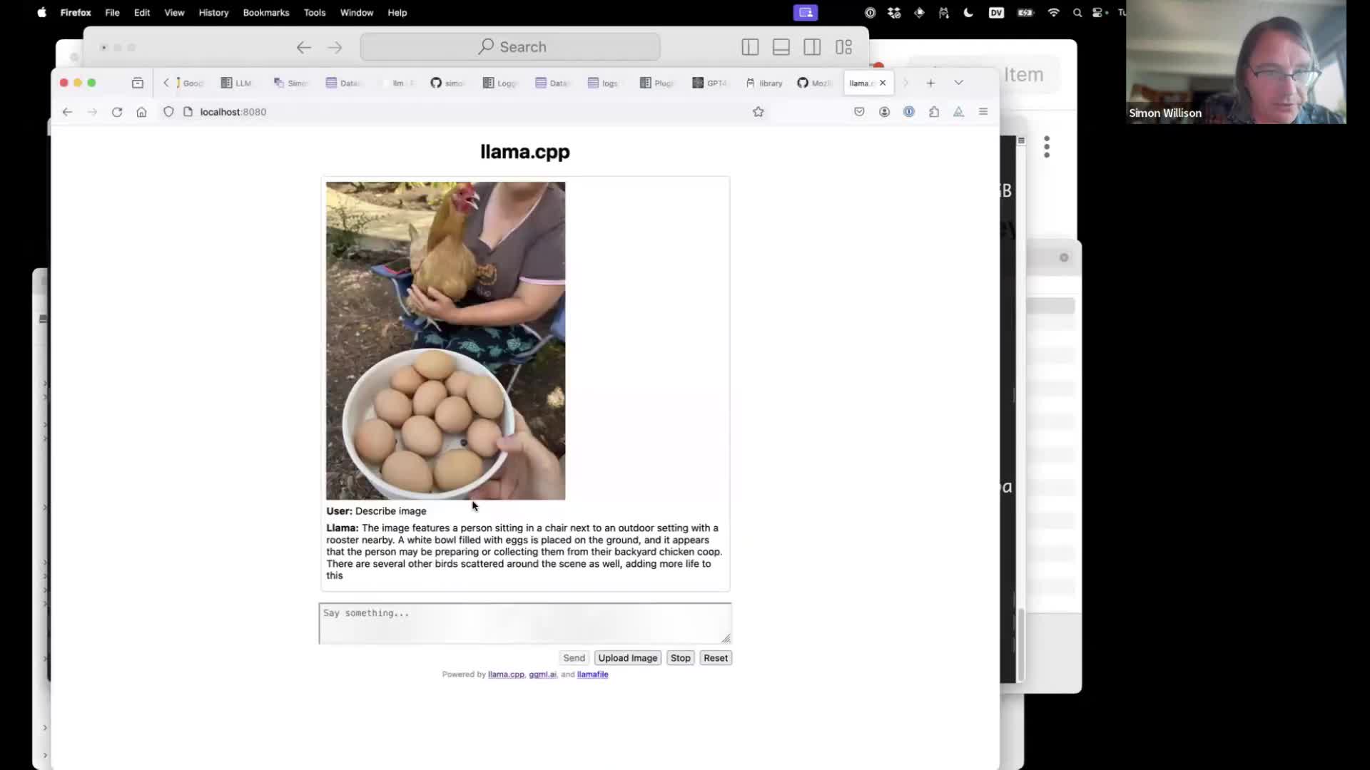 Screenshot of a browser window titled llama.cpp showing a photograph User: Describe image Llama: The image features a person sitting in a chair next to an outdoor setting with a rooster nearby. A white bowl filled with eggs is placed on the ground, and it appears that the person may be preparing or collecting them from their backyard chicken coop. There are several other birds scattered around the scene as well, adding more life to this